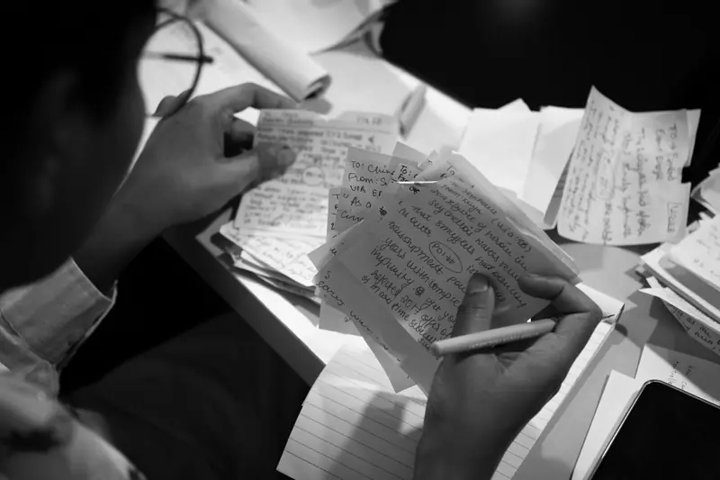 Black-and-white photo of hands sorting a pile of handwritten chits