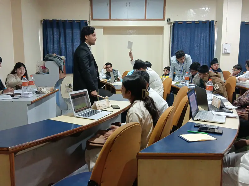 A delegate in a suit addresses a committee room as others raise placards